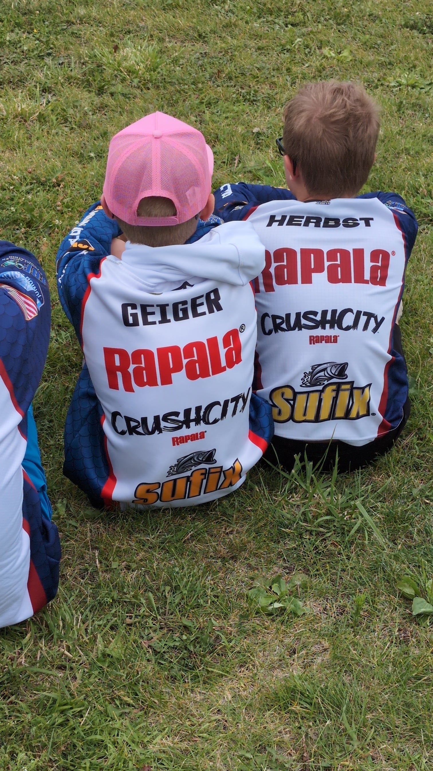 Two Junior BASS Nation anglers in tournament jerseys, sitting in the grass