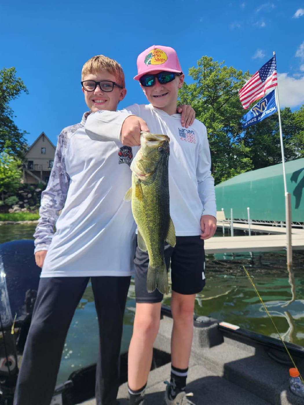 Two kids holding a bass by the flag at the dock