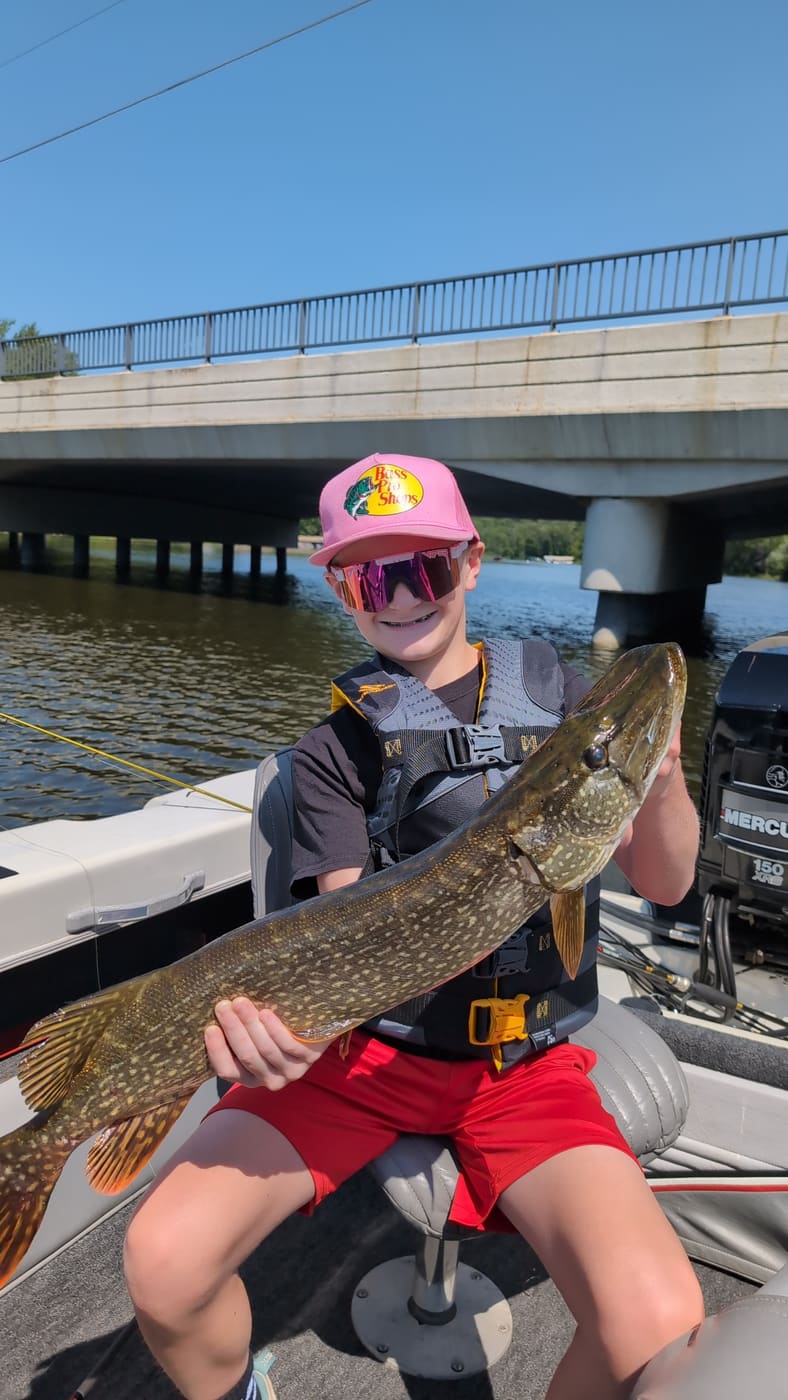 Kid in a pink hat holding a northern pike
