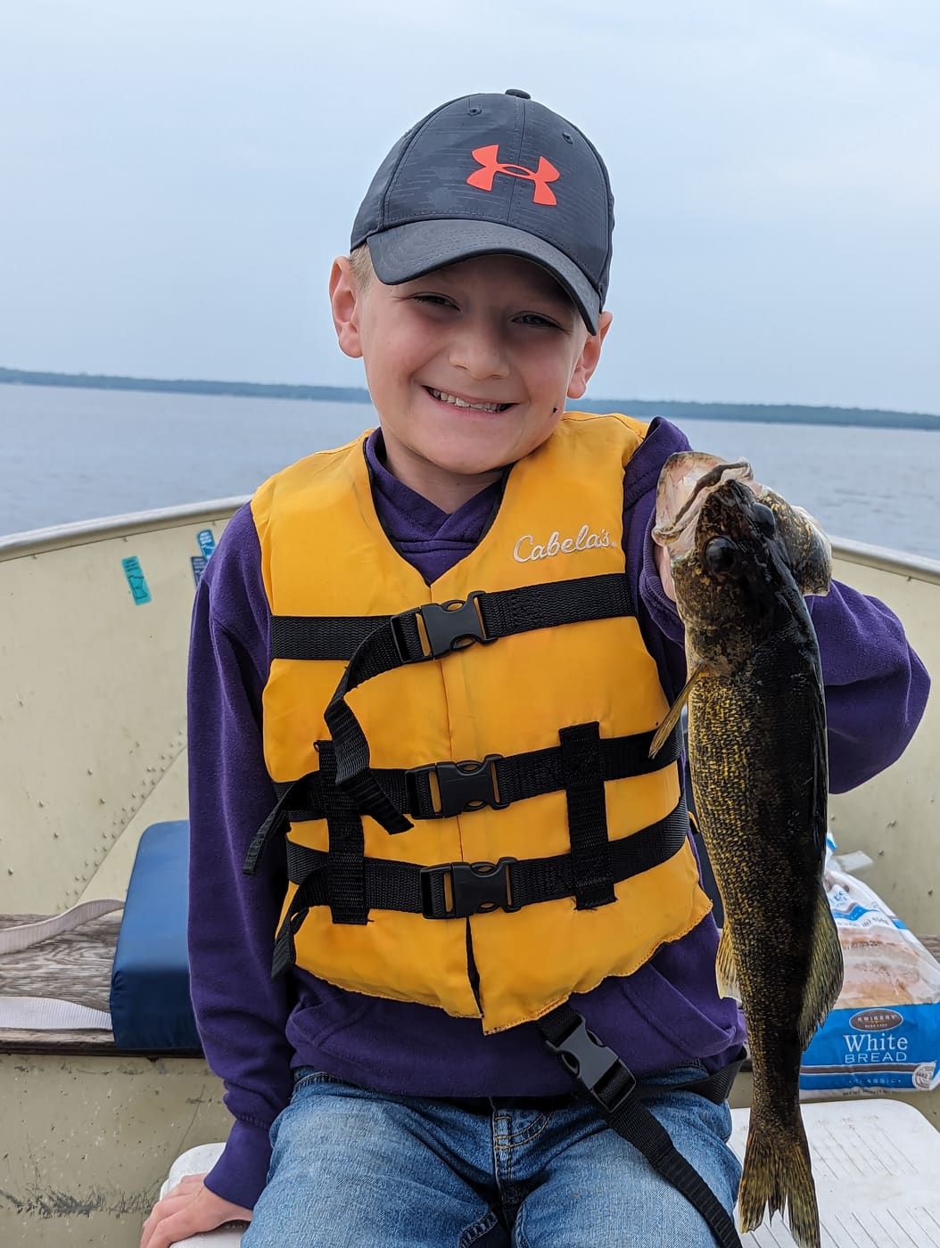 Young angler in a purple shirt and life jacket holding a walleye