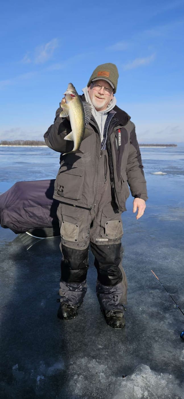 Angler in a Passive Fishing beanie holding a walleye on the ice